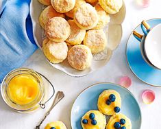 blueberry muffins and orange juice are on plates next to two cups of tea