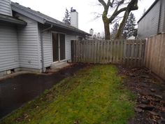 a fenced in yard next to a house with trees and grass on the ground