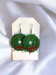 green crocheted wreath earrings with red ribbon and bow on white cardigane