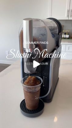 a coffee maker sitting on top of a counter next to a cup filled with liquid