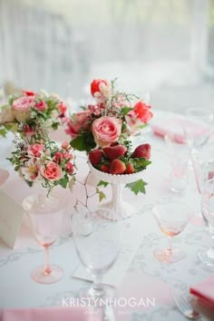 the table is set with pink flowers and white vases filled with strawberries, roses, and greenery