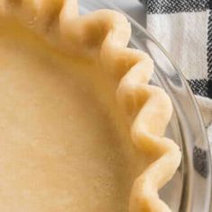 an uncooked pie crust sitting on top of a glass plate next to a checkered napkin