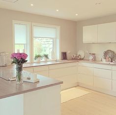 a kitchen with white cabinets and pink flowers in a vase on the island countertop