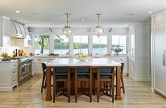 a large kitchen with an island table surrounded by blue chairs and white cabinetry, along with windows overlooking the water