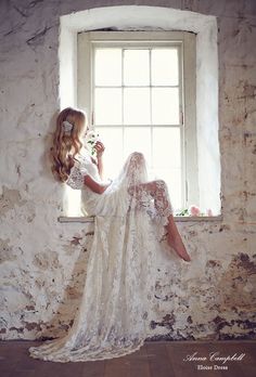 a woman sitting on a window sill in front of a white brick wall and holding a flower