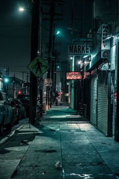 an alley way with cars parked on the side and street signs lit up at night