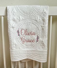 a white crib with a quilt hanging on it's side and the words julia grace written in pink