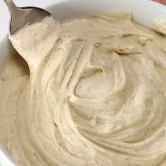 a white bowl filled with hummus sitting on top of a wooden table next to a spoon