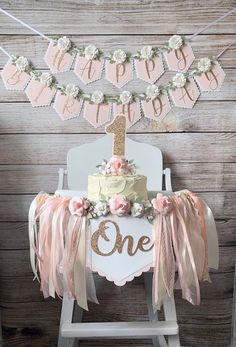 a birthday cake on top of a chair with pink and gold decorations hanging from it