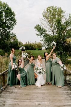 a group of bridesmaids posing on a bridge with their bouquets in the air