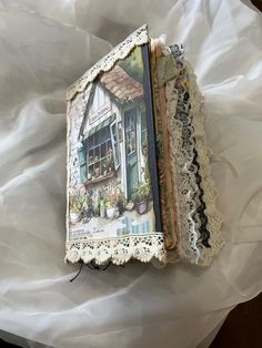 an open book with lace on it sitting on top of a white cloth covered bed