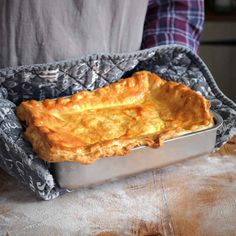 a baked dish in a metal pan on a wooden table with a person standing behind it