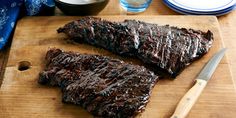 two pieces of barbecue ribs on a cutting board with a knife and bowl next to it