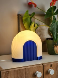 a blue and white light sitting on top of a wooden dresser next to a potted plant