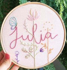 someone is holding up a embroidery hoop with the word julia written in pink and blue