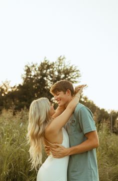 a young man and woman embracing each other in the middle of a field with tall grass