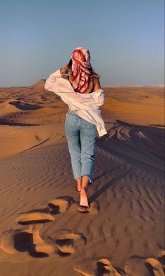 a woman walking in the desert with her scarf over her head and writing on the sand