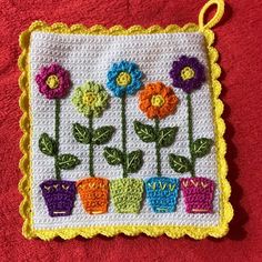 a crocheted flower pot holder with flowers in it on a red towel next to a pair of scissors