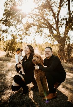 a man and woman holding a dog pose for a photo in front of some trees