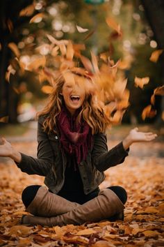 a woman sitting on the ground with her hands in the air and falling leaves around her