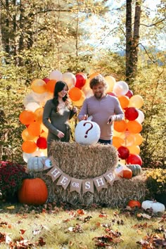 a man and woman standing in front of a hay bale with balloons on it