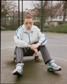 a man sitting on top of a skateboard in front of a tennis court with his legs crossed