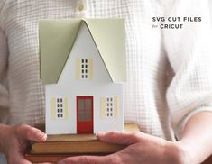 a person holding a paper model of a house with red door and windows in their hands