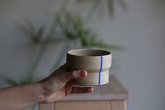 a hand holding a small cup with blue lines on it's side, in front of a plant