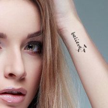 a woman with a tattoo on her arm holding her hand up to her head and looking at the camera