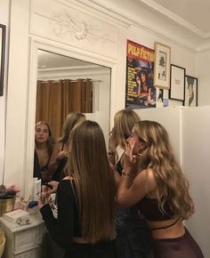 three women standing in front of a mirror brushing their teeth