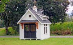 a small white and black shed sitting on top of a lush green field next to trees