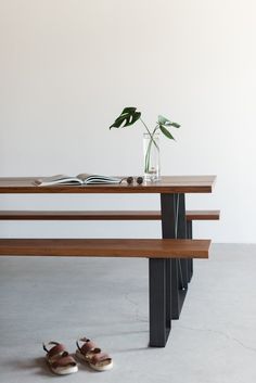 a pair of shoes sitting on the ground next to a table with a book and vase