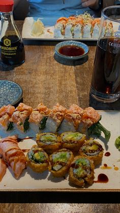 sushi rolls and sauces on a wooden table with people sitting at the table