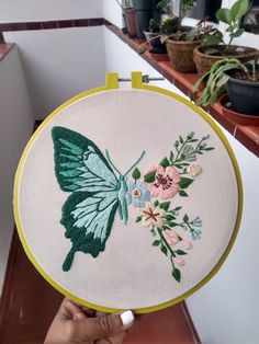 a person holding up a green and white embroidered butterfly with flowers on it's back