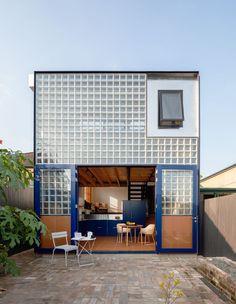 an open patio with chairs and tables in front of a house that is made out of glass blocks