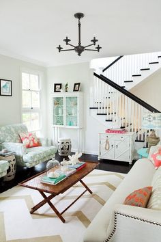 a living room filled with furniture next to a stair case in a white walled house