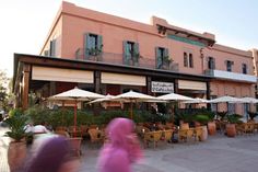 people are sitting at tables outside in front of a pink building with white umbrellas