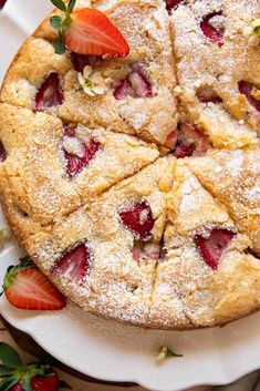 a strawberry cake with powdered sugar and sliced strawberries on the top, sitting on a white plate