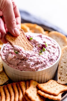 a hand dipping a cracker into a bowl of dip