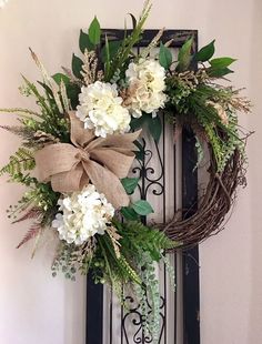 a wreath with white flowers and greenery hangs on a door frame in front of a wall