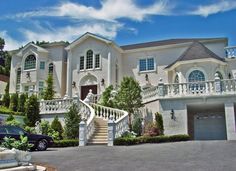 a large white house with stairs leading up to it's front door and two cars parked in the driveway