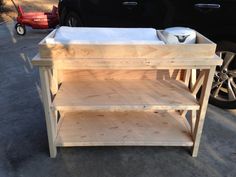 a small wooden table sitting on the side of a road next to a black car