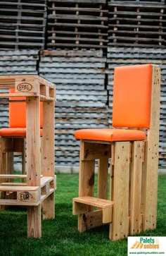 two wooden stools with orange cushions sit in the grass next to an empty chair