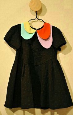 a black dress with multi colored collars hanging on a wall next to a wooden hanger