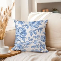 a blue and white flowered pillow sitting on top of a couch next to a cup