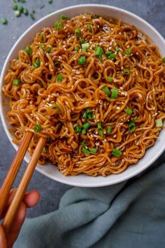 someone holding chopsticks over a bowl of noodles with sesame seeds and scallions