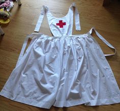 a white dress with a red cross on the chest and straps is sitting on a wooden floor