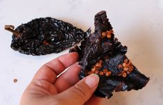 a hand holding some kind of food on top of a white counter next to another piece of chocolate