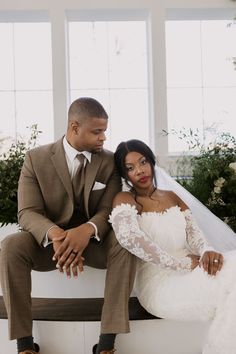 a bride and groom sitting on a bench in front of large windows at their wedding