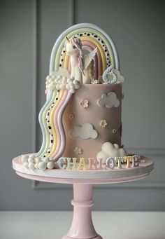 a pink cake with white frosting and rainbows on top is sitting on a pedestal